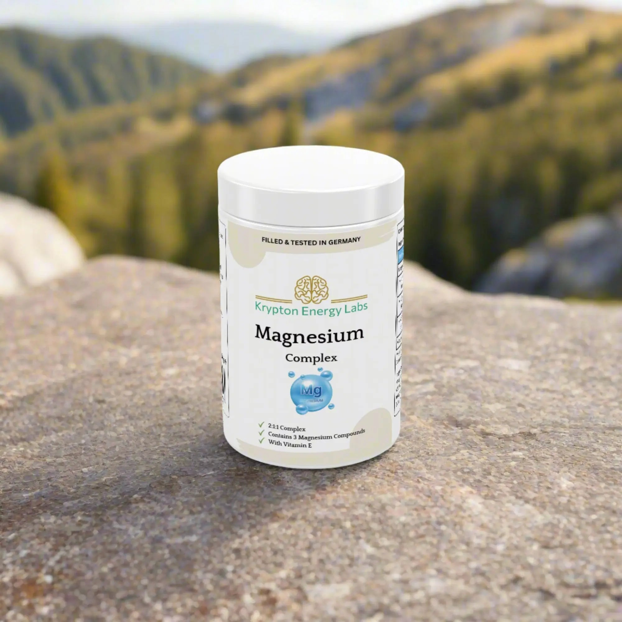 A bottle of Krypton Energy Labs' Magnesium Complex is set on a rock outdoors, against a blurred backdrop of rolling hills and lush greenery. The label reveals that it contains magnesium (Mg), Vitamin B, and other magnesium compounds designed to support muscle function and boost energy production, all meticulously filled and tested in Germany.