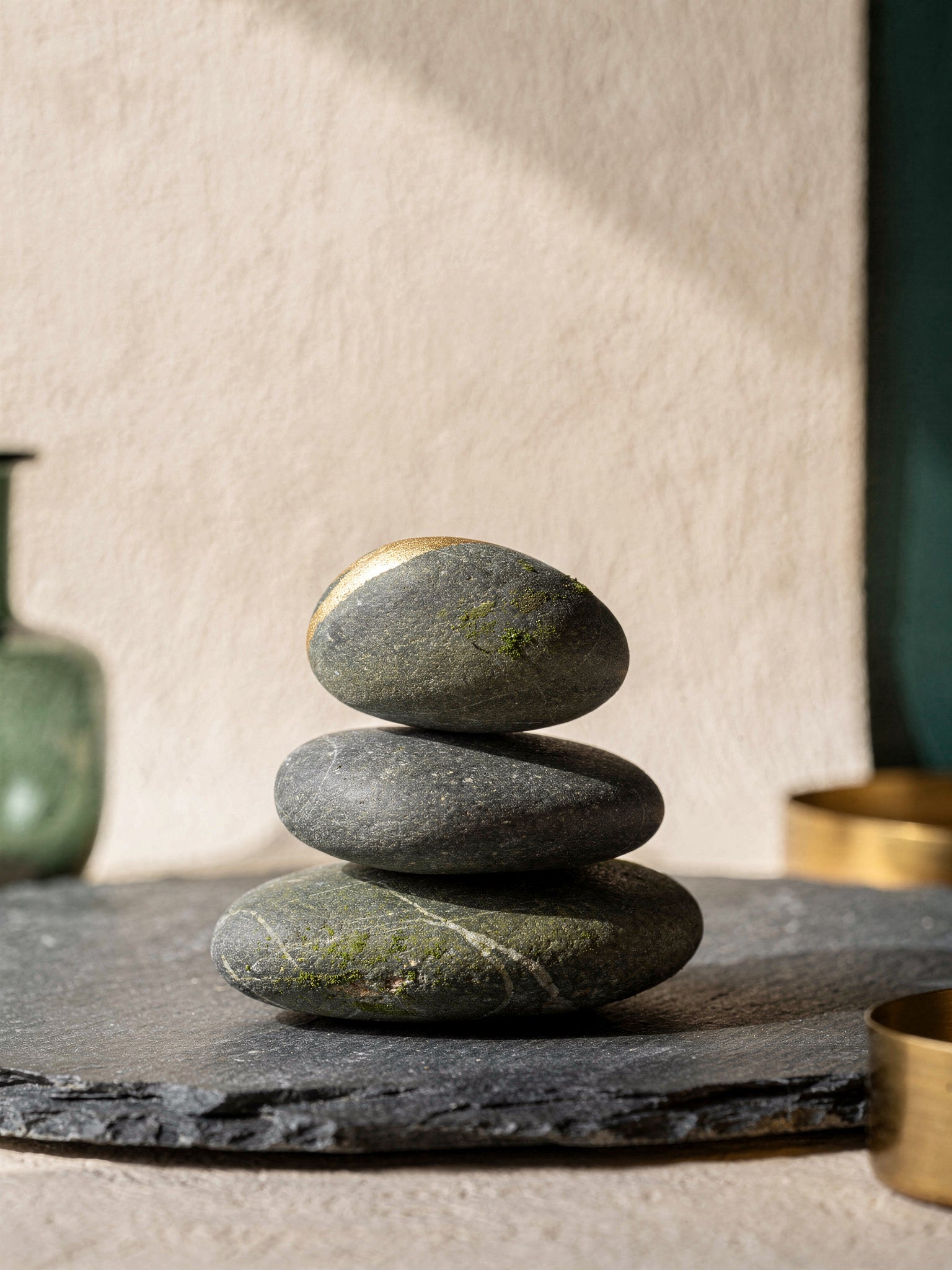 A cairn of three smooth river stones stacked in graceful balance on a slate surface, soft golden light catching the top stone.